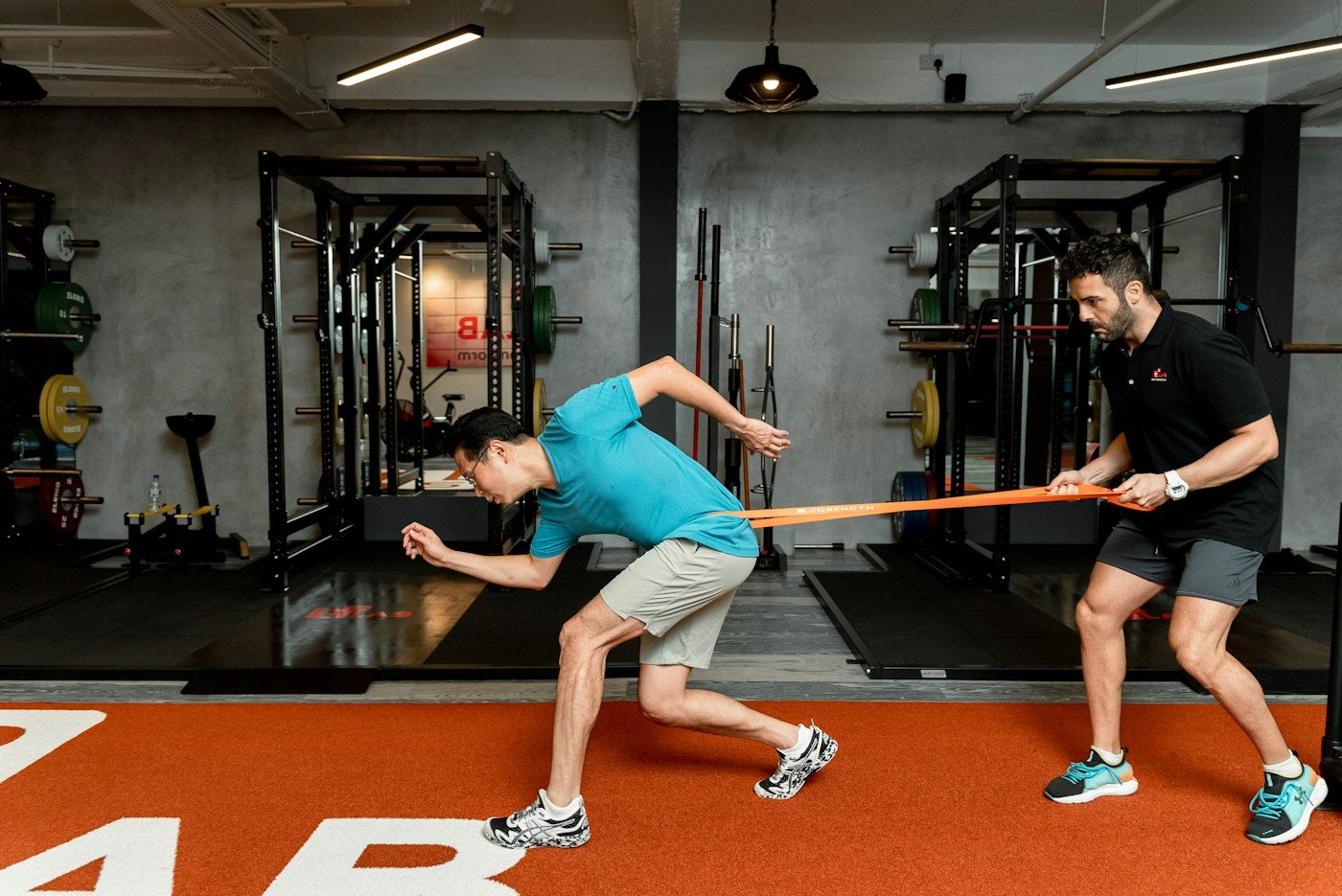 Athlete sprinting against a resistance band held by a trainer in a gym